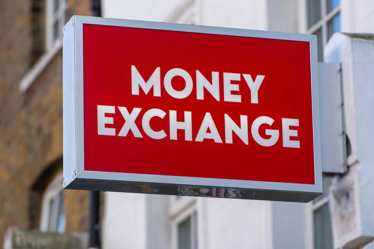 Person counting foreign bills at an airport exchange booth wondering do currency exchanges charge fees