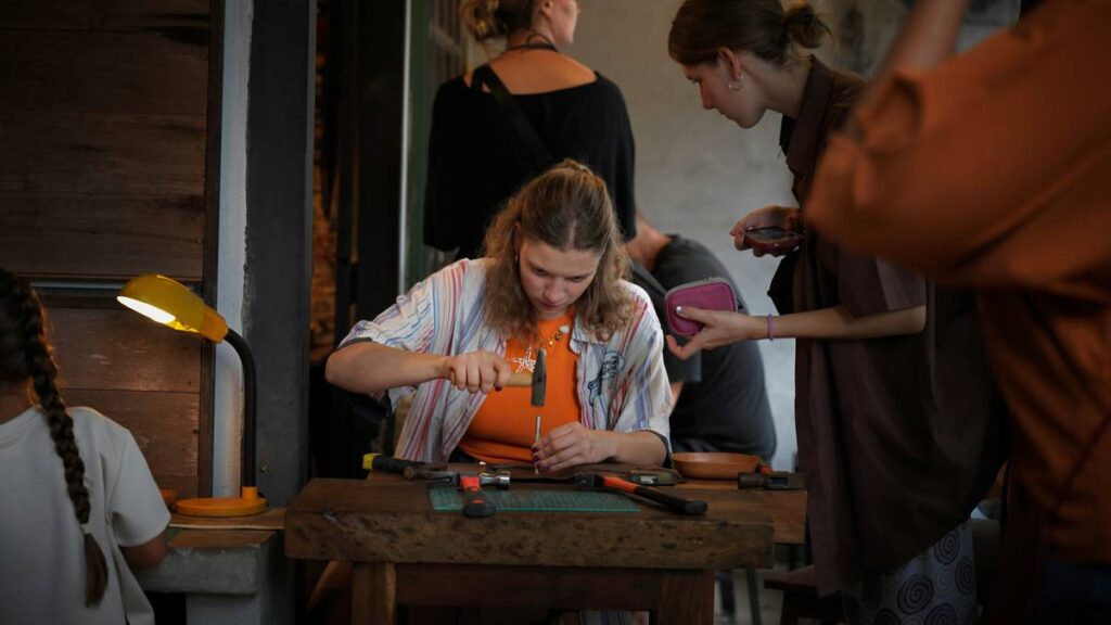 A woman hammering a metal tool into leather at a wooden workbench