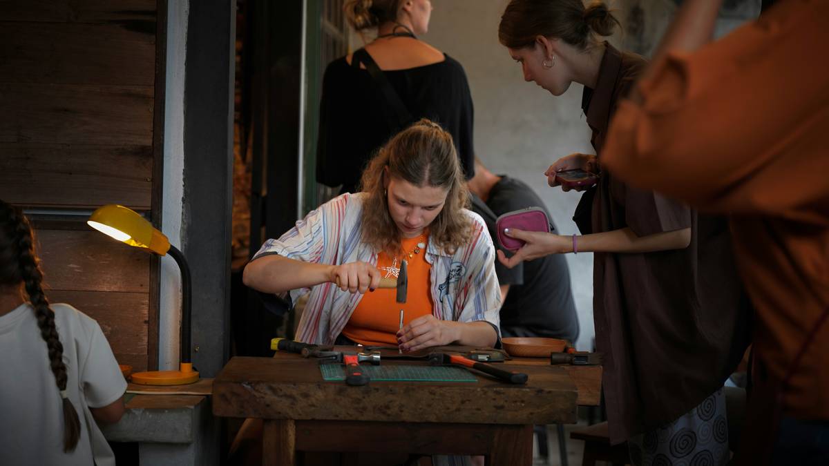 A woman hammering a metal tool into leather at a wooden workbench